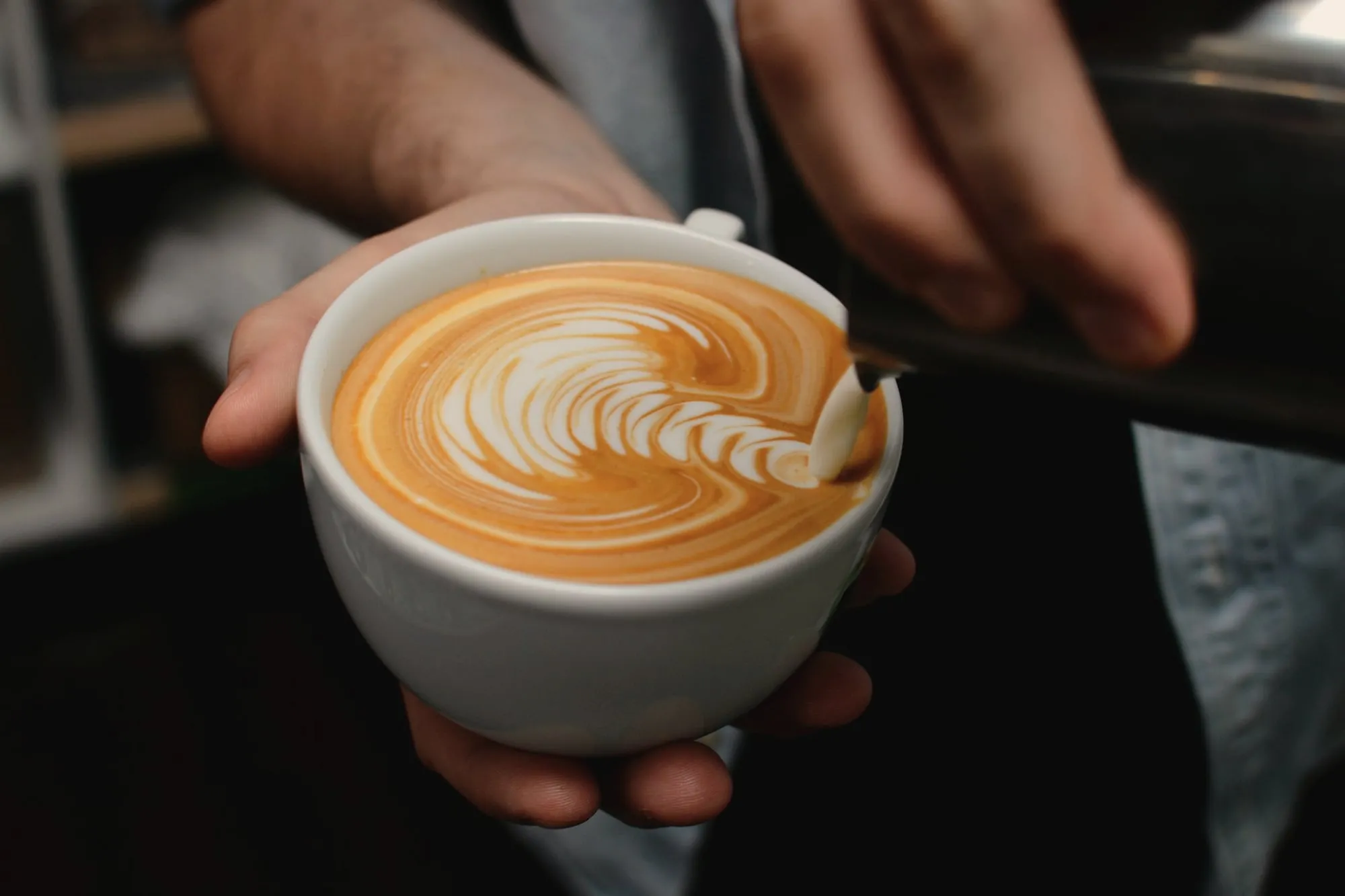 A flat white with a leaf pattern, held out in both hands